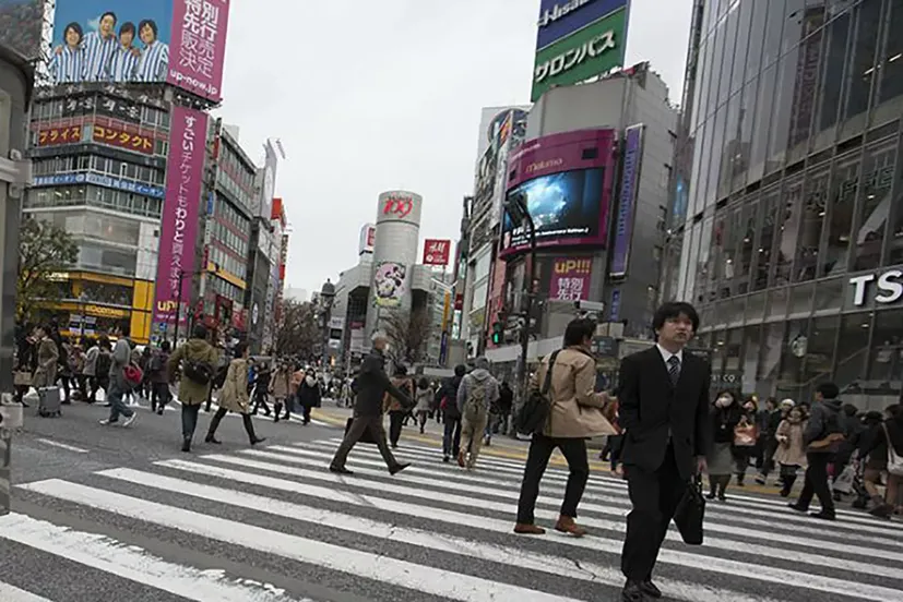People crossing an intersection in Japan with businesses in background